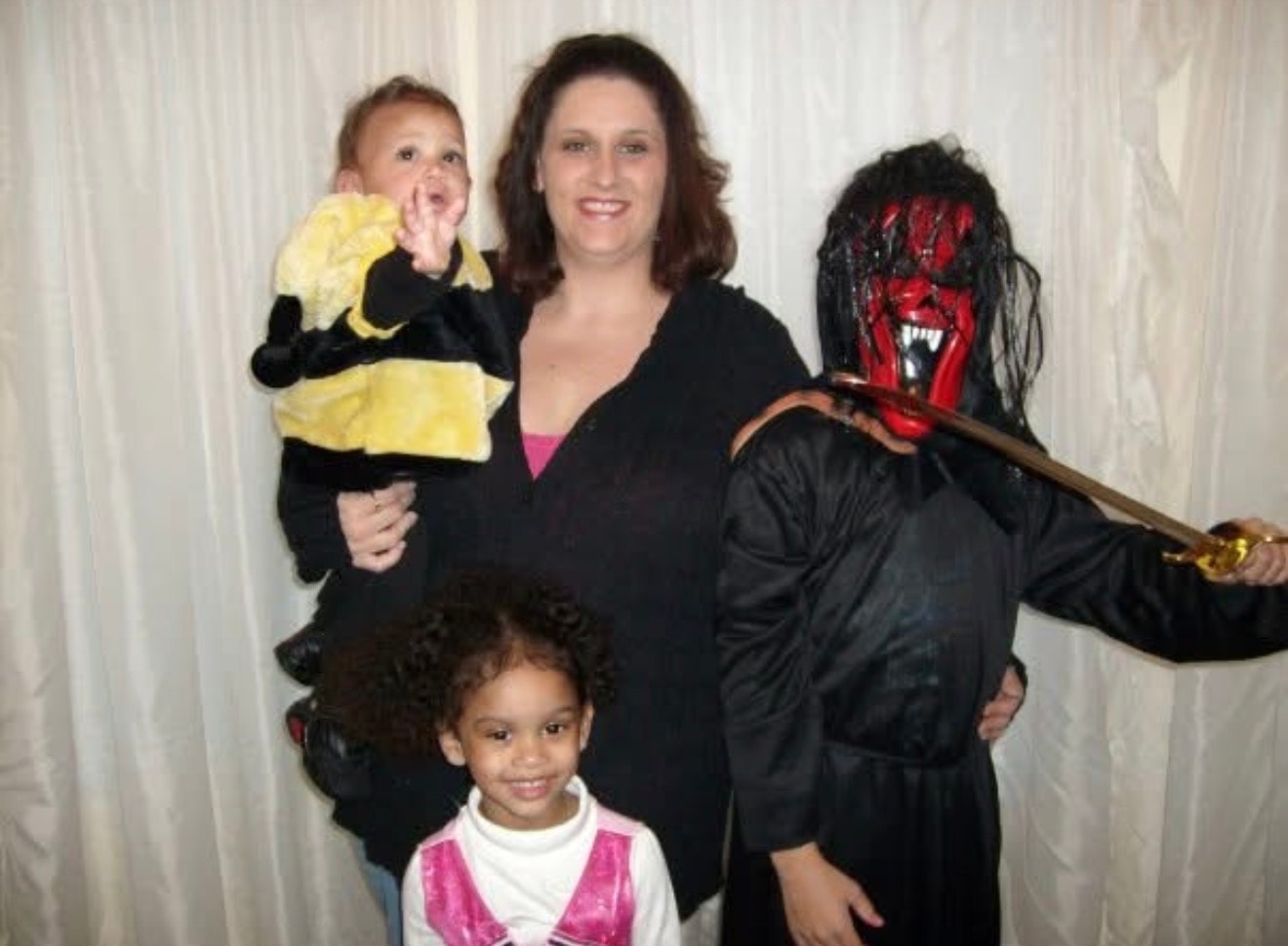 Meranda posing with three children in Halloween costumes in front of a white curtain.